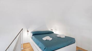 Ein Einzelbett mit blauer Bettdecke, weißen Kissen und zusammengerollten Handtüchern.