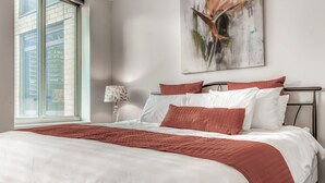 A neatly made bed with white and red bedding, a modern lamp, and a large abstract painting on the wall. - Global Luxury Suites in Abilene Texas (Abilene)