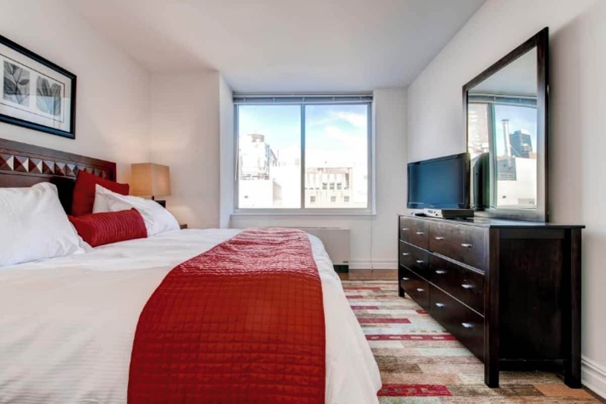 Habitación de hotel con una cama grande, un tocador, una televisión y una ventana con vistas a la ciudad.