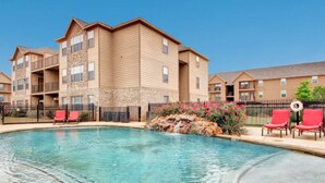 A hotel with a swimming pool, red lounge chairs, and a stone waterfall feature. - Global Luxury Suites in Abilene Texas (Abilene)