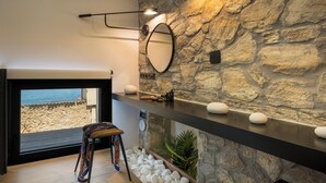 Une salle de bain moderne avec un mur en pierre, un grand miroir et une étagère ornée de pierres décoratives.