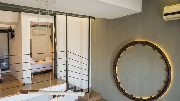 Un appartement moderne de style « loft », doté d’un lit en mezzanine, d’une table à manger en bois, d’un canapé intégré et d’un grand miroir rond accroché au mur.
