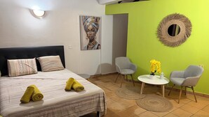 Ein Hotelzimmer mit einem Bett, zwei Stühlen, einem kleinen Tisch mit Blumenvase und einem Wandspiegel.