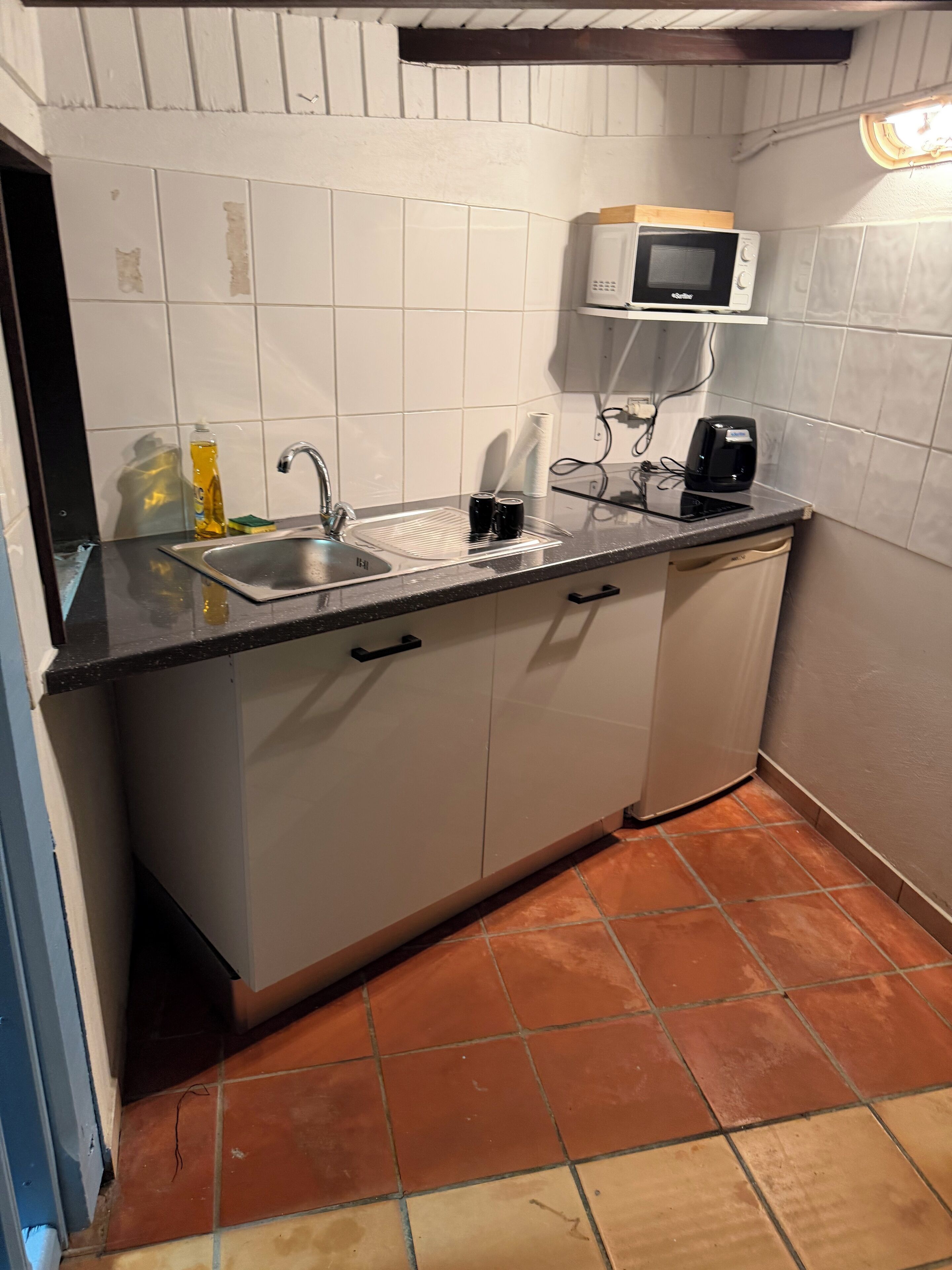 A kitchen with white cabinets, a black countertop, a sink, a microwave, and a coffee maker.