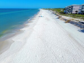 Ein Strand mit blauem Himmel, sandigem Ufer und einem Gebäude mit mehreren Balkonen.