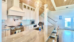 A modern kitchen with a marble island, stainless steel appliances, and pendant lighting. - Luxury, old-Florida charm, N. Cape gulf front, outdoor TV, pvt beach access (Port Saint Joe, FL)