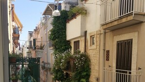 A narrow street with buildings on either side, featuring balconies with railings and some greenery. - [Casa Camelia] Elegant Palace with Terrace (Conversano)