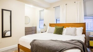 Una camera da letto con un letto di legno, uno specchio, una cassettiera e una finestra con tende.