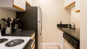 Una cucina compatta con piano cottura, frigorifero, lavastoviglie e macchina per il caffè.
