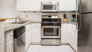 A modern kitchen with white cabinets, stainless steel appliances, a granite countertop, and a tiled floor. - The only 4 Bedroom Apartment w/ Roofdeck in Boston!  8min from Fenway Park, close to universities! (Boston)