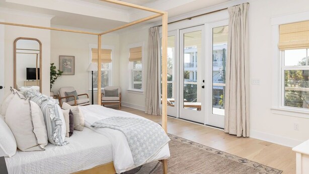 Une chambre à coucher avec un lit à baldaquin, un grand miroir, une chaise, un bureau et une vue sur l’extérieur grâce aux portes-fenêtres coulissantes.