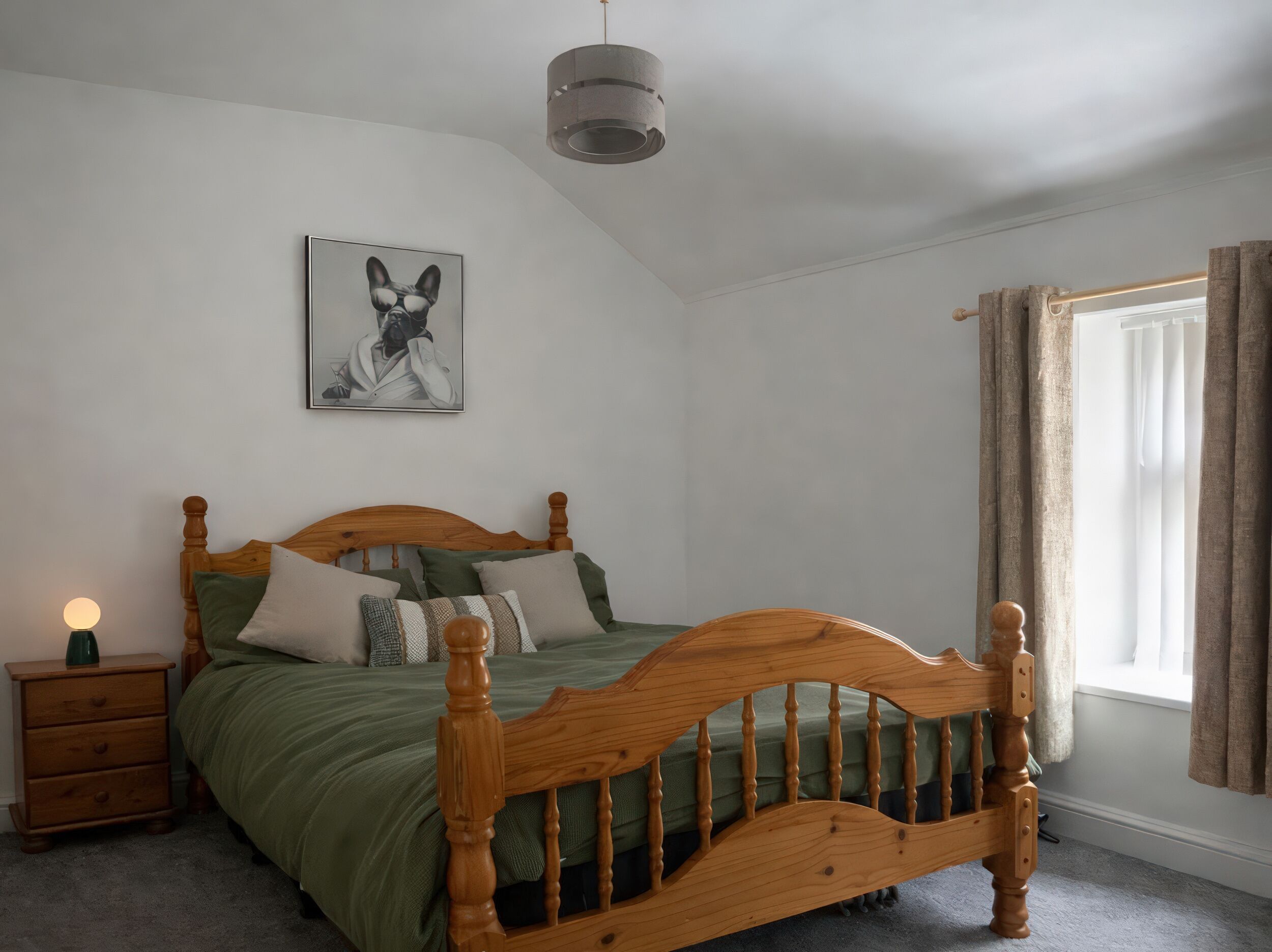 Un dormitorio con una cama de madera, una mesita de noche, una lámpara, un cuadro en la pared y una ventana con cortinas.