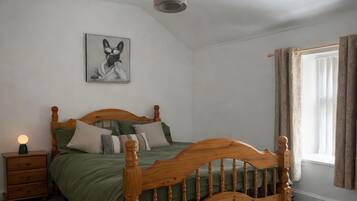 Un dormitorio con una cama de madera, una mesita de noche, una lámpara, un cuadro en la pared y una ventana con cortinas.