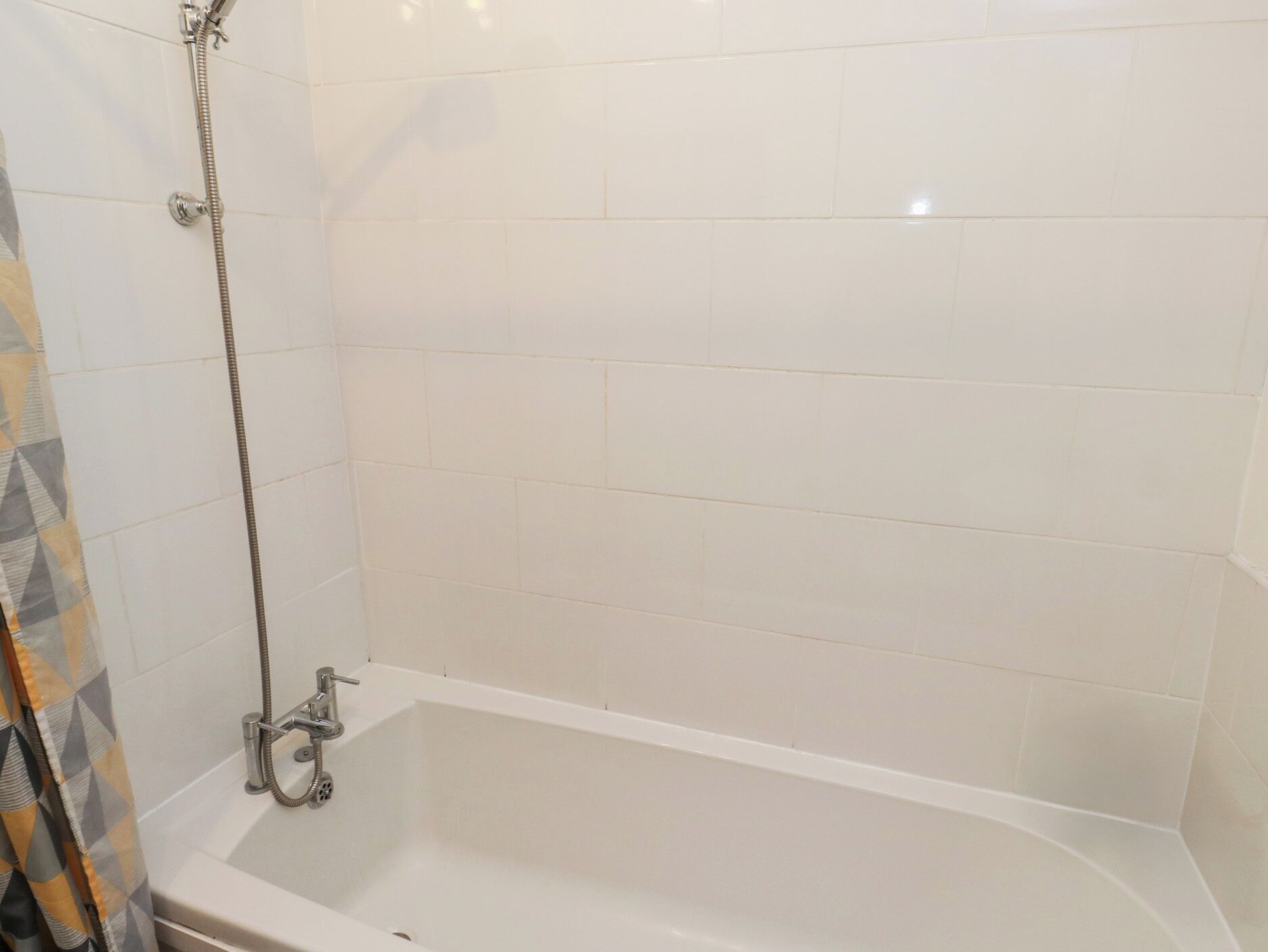 Een badkamer met witte betegelde wanden, een badkuip en een douchekop.