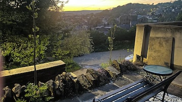 Eine Bank mit gemustertem Unterleger, eine Steinmauer und Blick auf ein Wohngebiet bei Sonnenuntergang.