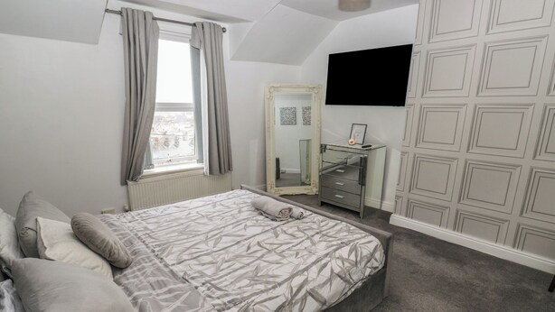 Ein Schlafzimmer mit einem Bett, einem Schminktisch, einem Spiegel und einem an der Wand befestigten Fernseher.