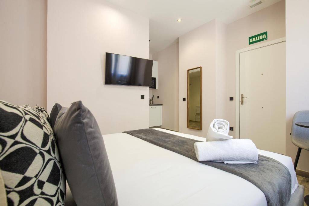 Een hotelkamer met een bed, een aan de muur bevestigde televisie, een spiegel, een deur met de aanduiding 'SALIDA' en een handdoek op het bed.