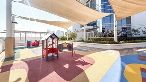 A rooftop playground with play structures and a view of a modern building. - StayShort - Studio in Damac Hills that Sleeps 3 with Terrace! (Damac Hills)