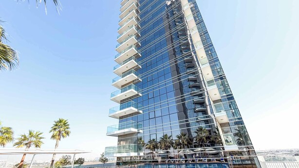 A high-rise building with a glass facade and a rooftop pool area. - StayShort - Studio in Damac Hills that Sleeps 3 with Terrace! (Damac Hills)
