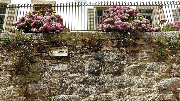 A white building with multiple windows and shutters, a stone wall with a sign reading "Bois d'Amiour," and pink flowers in front. - Kermaria Trois Fontaines Deluxe Studio Suite, by the Bois d’Amour Pont Aven (Pont-Aven)