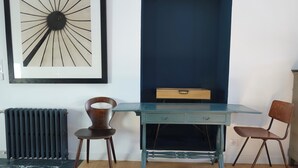 A room with a blue desk, two wooden chairs, a radiator, and a framed abstract artwork on the wall. - Kermaria Trois Fontaines Deluxe Studio Suite, by the Bois d’Amour Pont Aven (Pont-Aven)