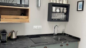 A kitchen with a built-in microwave, a coffee maker, a sink, and a shelf with cups and glasses. - Kermaria Trois Fontaines Deluxe Studio Suite, by the Bois d’Amour Pont Aven (Pont-Aven)