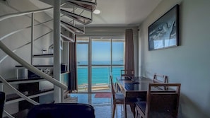 A room with a spiral staircase, a dining area with a view of the sea, and a painting on the wall. - Duplex penthouse in the Porto Real Condominium.   (Mangaratiba)