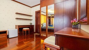 Una stanza con pavimento in legno, una scrivania, una sedia, un armadio e un letto con uno specchio.