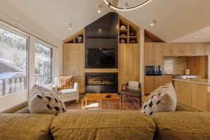 Ein modernes Wohnzimmer mit Kamin, Holzausbau und einem großen Fenster mit Blick auf eine Terrasse.