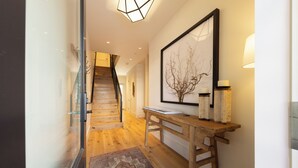 Ein Flur mit einer Holztreppe, einem gerahmten Kunstwerk, einem Tisch mit Kerzen und einem gemusterten Teppich.