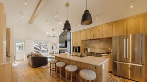 Eine moderne Küche mit Holzausstattung, einem Edelstahl-Kühlschrank, einer Bar mit Sitzgelegenheiten und einer großen Kücheninsel.
