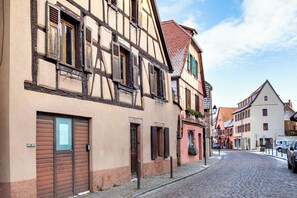 A cobblestone street lined with traditional half-timbered buildings, featuring wooden shutters and a mix of open and closed doors. - 177 m² family home in the heart of the vineyards! (Kaysersberg Vignoble)