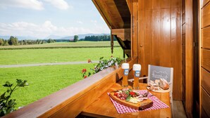 A wooden bench with a table set for a meal, overlooking a green field and mountains. - Hussnhof Farm Lodge (Sachsenkam)