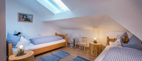 A cozy attic bedroom with a skylight, two beds with checkered bedding, a small table with a lamp, and a framed picture on the wall.