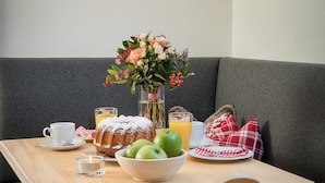 A dining table with a vase of flowers, a bowl of apples, a glass of orange juice, and a plate of food. - Hussnhof Farm Lodge (Sachsenkam)