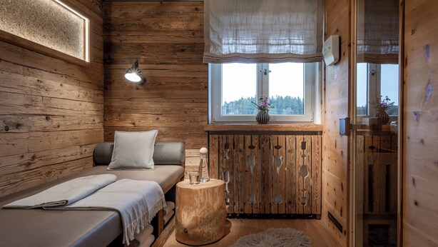 A cozy cabin-style room with a wooden interior, a bed, a small table with a vase, and a window with a view of trees. - Hussnhof Farm Lodge (Sachsenkam)