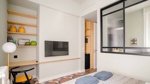 A compact bedroom with a bed, a TV mounted on the wall, a small desk with a chair, and a window with blinds. - Room-central Design Room - Private Bathr (Milan)