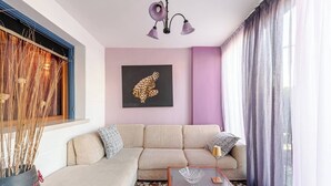 Un salón con un sofá color beige, una mesa de centro de vidrio y una lámpara de pared.