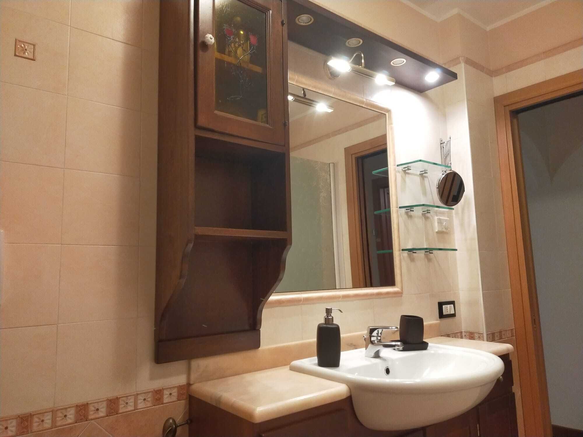 Une salle de bain avec un grand miroir, un lavabo et une étagère en verre où sont rangés les articles de toilette.