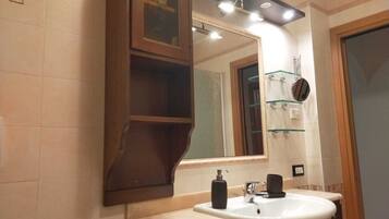Une salle de bain avec un grand miroir, un lavabo et une étagère en verre où sont rangés les articles de toilette.