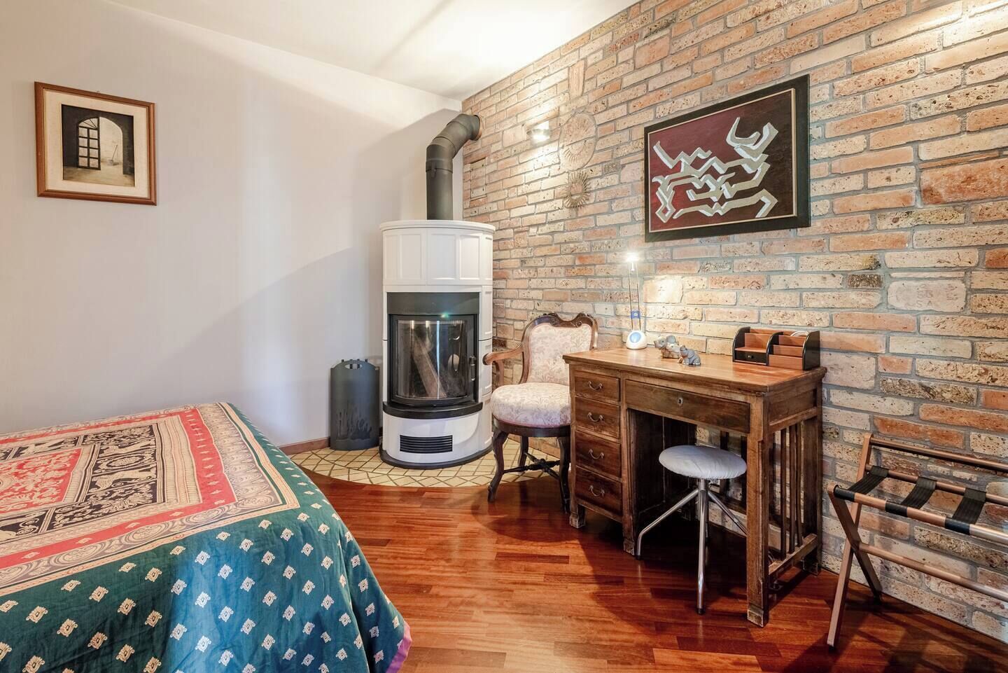 Ein gemütliches Zimmer mit Kamin, einem Holztisch, einem Stuhl und einem Bett mit gemusterten Betttextilien.