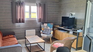 A cozy living area with a sofa, a small table, a chair, a TV, and a wooden cabinet. - Charming chalet SAINT JACQUES SARZEAU GOLFE DU MORBIHAN - 330m² private garden (Sarzeau)