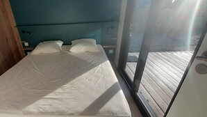 A small, single-bed room with a wooden headboard, a teal-colored wall, and a view of a wooden deck through a glass door. - Charming chalet SAINT JACQUES SARZEAU GOLFE DU MORBIHAN - 330m² private garden (Sarzeau)