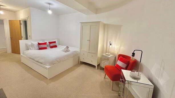 Un dormitorio con cama, armario, escritorio con silla y lámpara de noche.