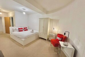 Un dormitorio con cama, armario, escritorio con silla y lámpara de noche.