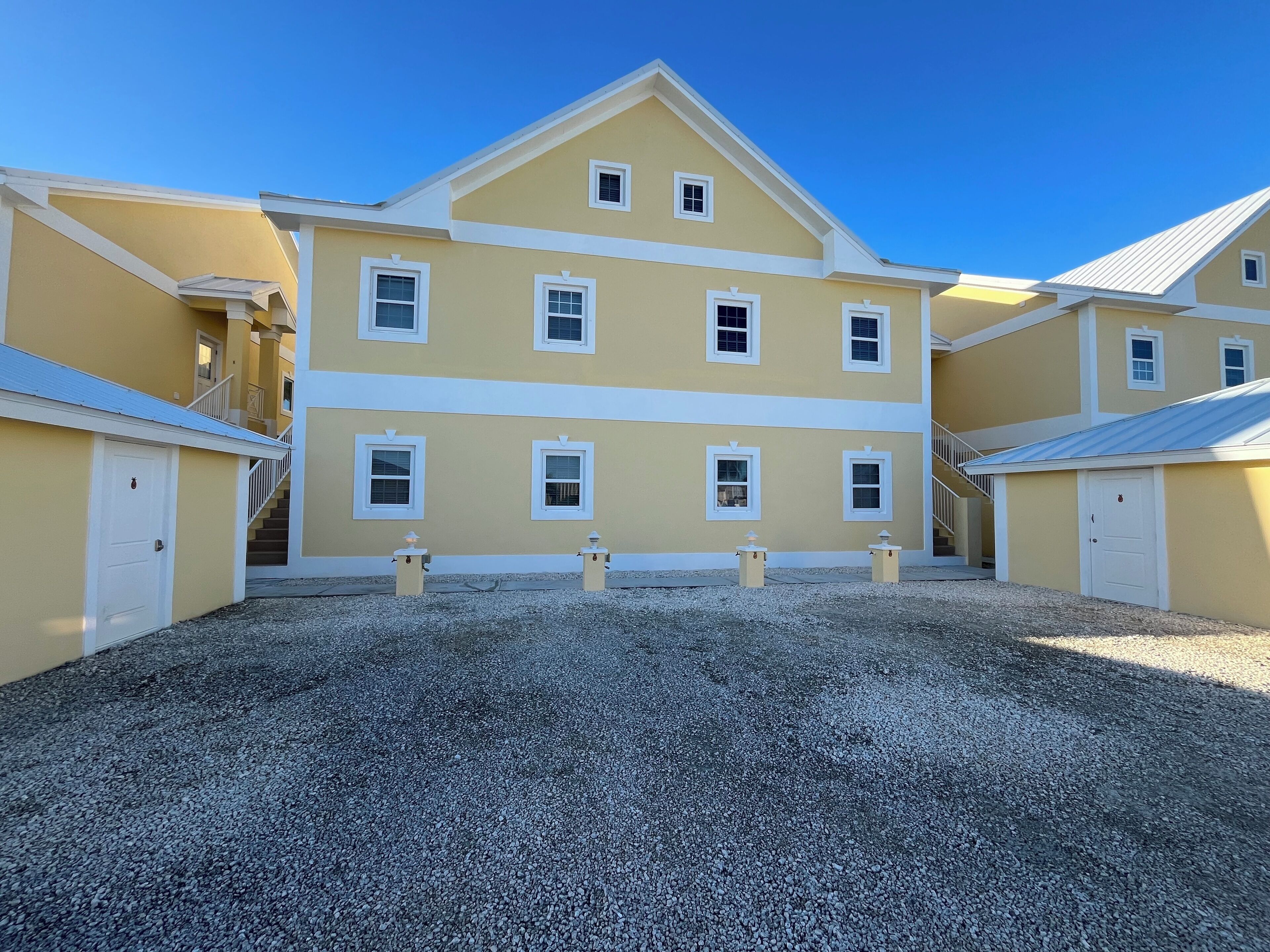 A multi-story yellow building with white trim, a gravel driveway, and a clear blue sky.