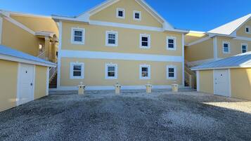 A multi-story yellow building with white trim, a gravel driveway, and a clear blue sky.