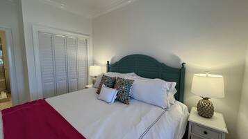 A neatly made bed with white linens and colorful pillows, a teal headboard, and two bedside lamps on white nightstands.