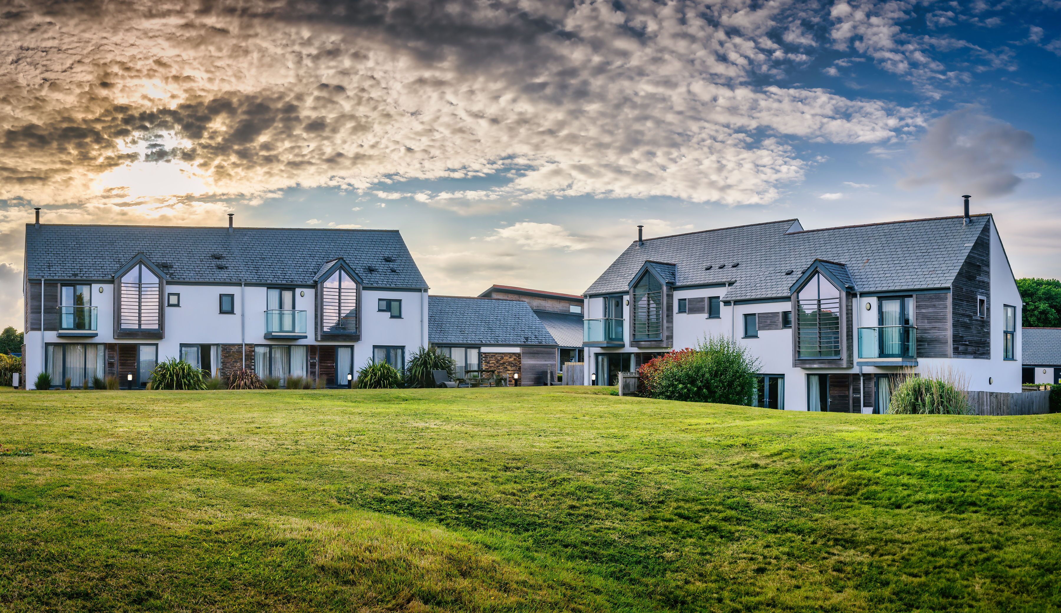 A modern residential area with two houses featuring large windows and balconies, surrounded by a well-maintained lawn.