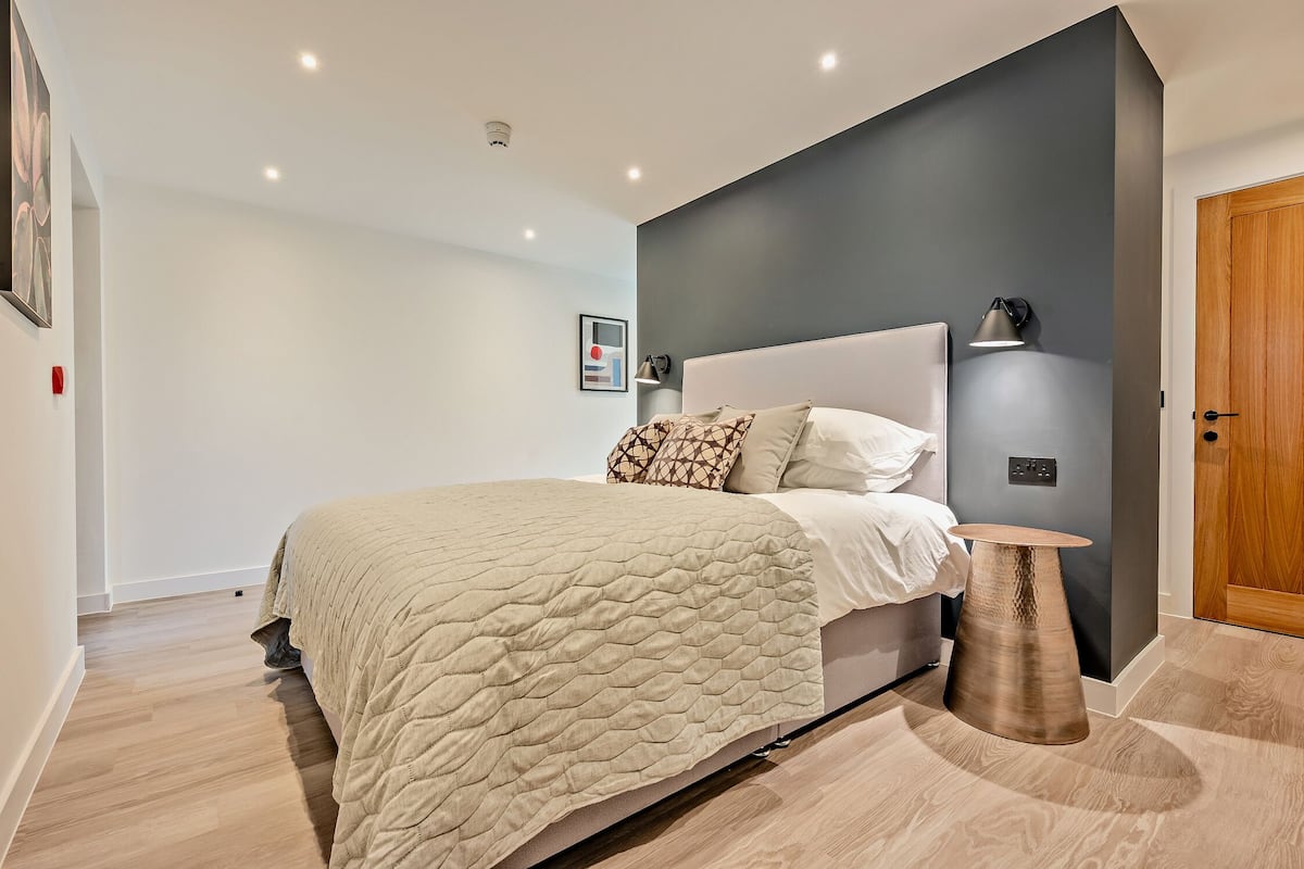 A modern bedroom with a large bed, a bedside table, and a wall-mounted lamp.